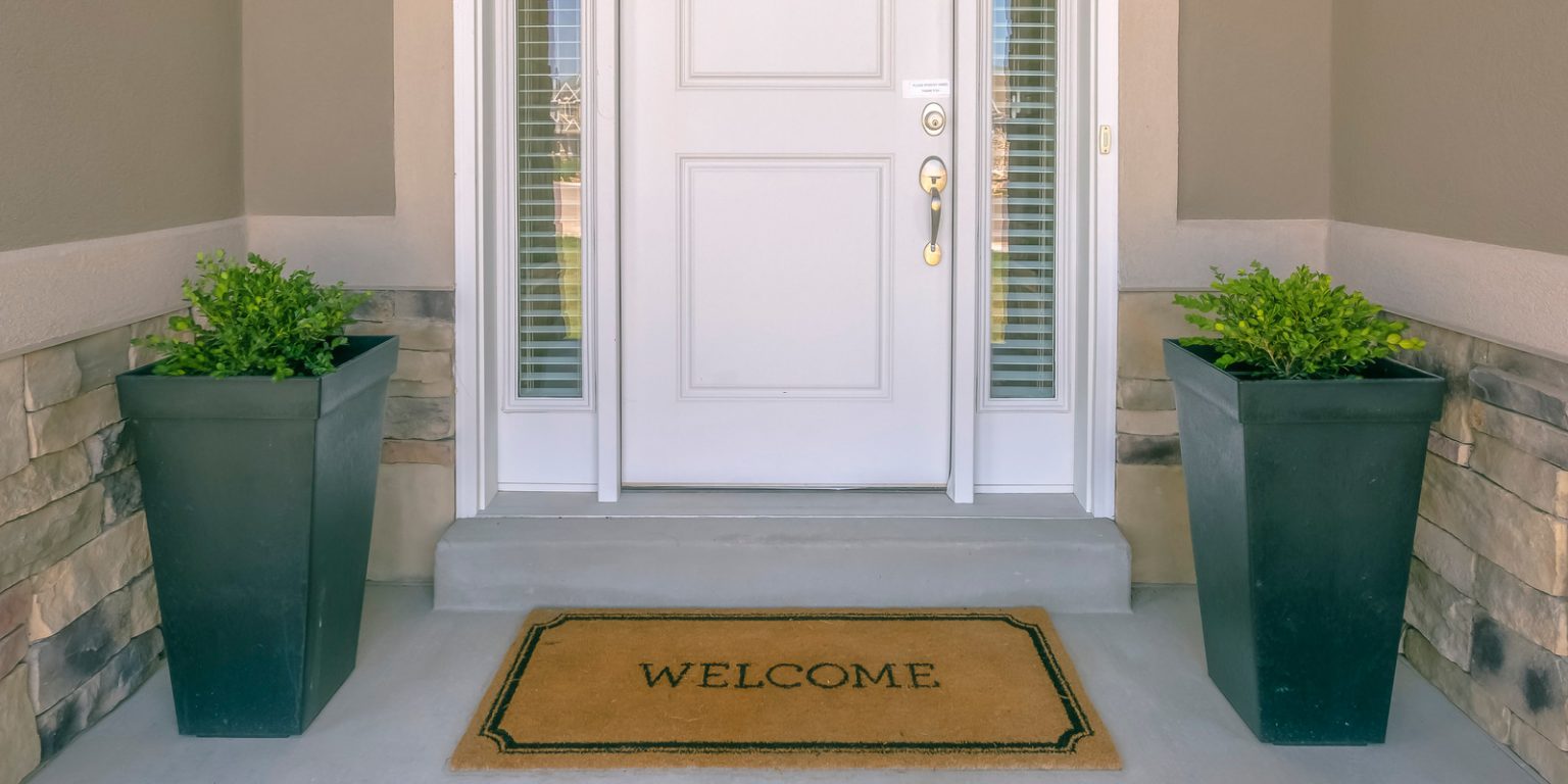 Covid-19 is a time of economic crisis – is now a good time to develop property? Alt="Front door with doormat plants and glass panel. White front door of a house with the word welcome printed on the brown doormat. Ornamental plants and glass panels are on each side of the door."