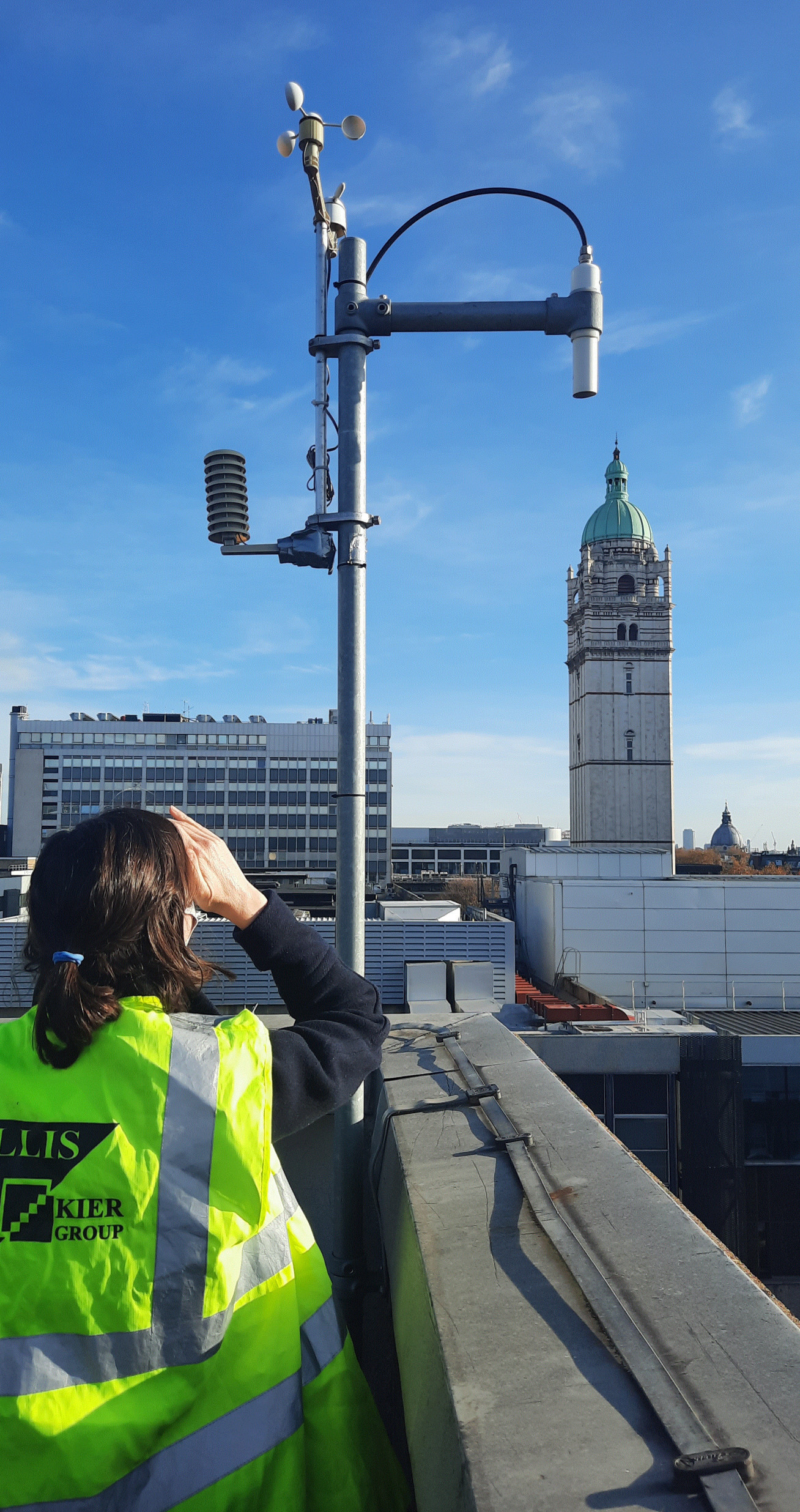 Woman looking at some equipment on a tall pole on top of a building