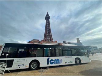 A white bus parked on the promenade in front of the Blackpool Tower