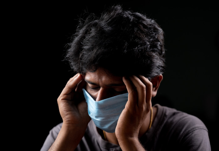 A person wearing a face mask and touching their temples in pain