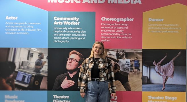 Performing Arts female student standing in front of the wall display