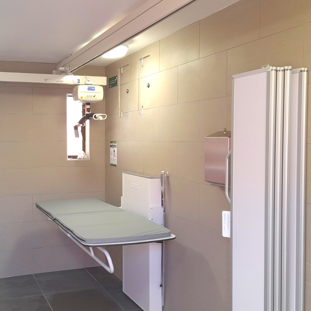 this shows the interior of the changing place, showing the adjustable bench, hoist and privacy screen