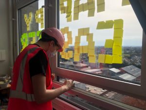 Fred looking out of his hospital window at the building site, wearing a hi-vis jacket and pink builders' helmet.