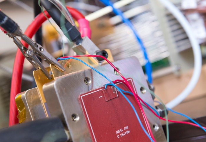 A photo of the fuel cell, made of metal layers, connected up to wires for testing in the lab