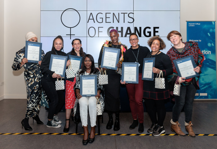 A group of women standing in front of a large screen hold certificates