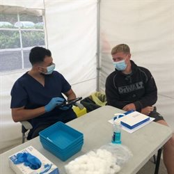 A health professional sits with a young male in a vaccination tent