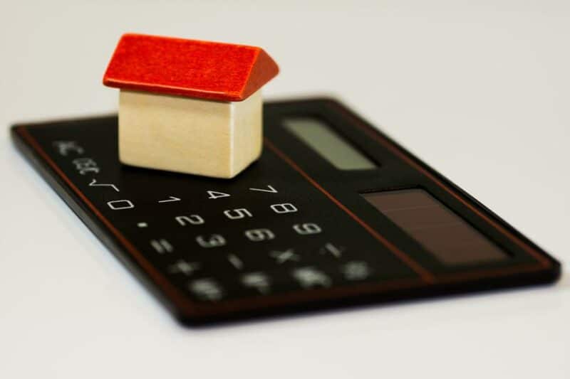 Image shows a tiny model of a house sitting on top of a calculator, to represent household costs