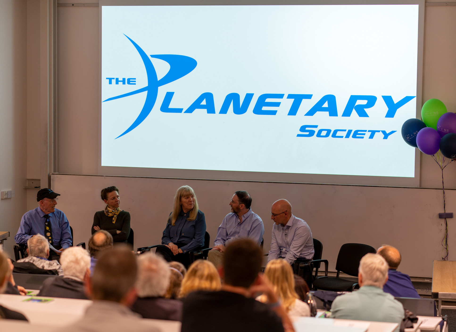 A group of panellists sit in front of an audience