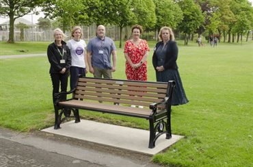 A group of people stood around a park bench