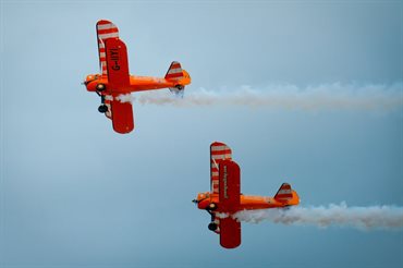 Two biplanes flying with trail of smoke.