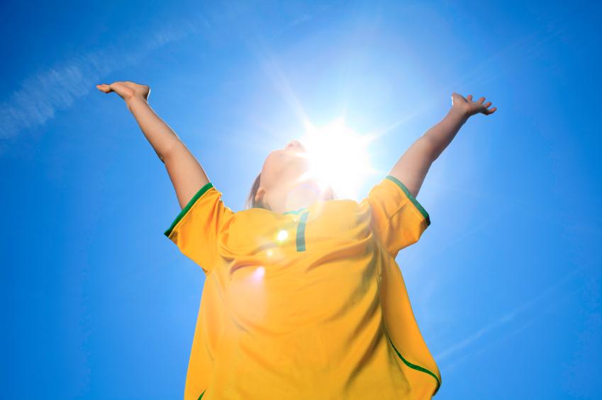 Here is a boy with his arms aloft with the sun shining brightly in the blue sky behind him