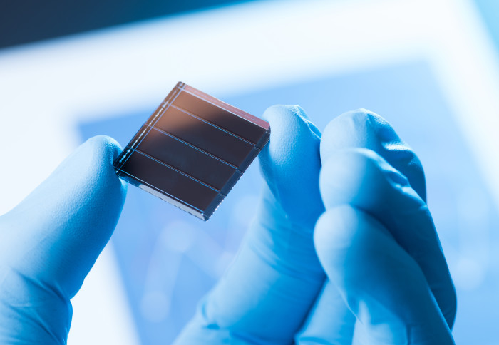 Gloved hand holding a small black solar cell between two fingers
