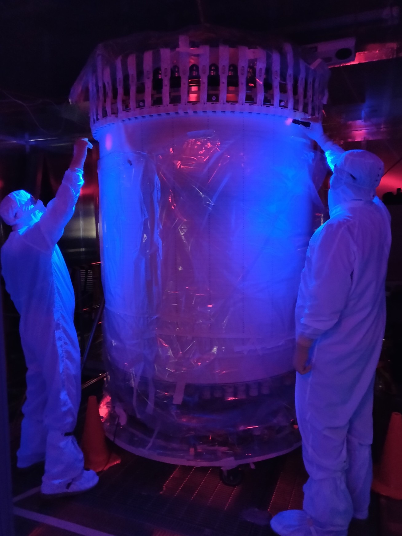 Two people in hazmat suits inspect a large cylinder with UV lights