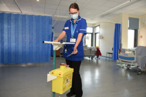 Deputy sister nurse putting needle in sharps bin attached to a trolley