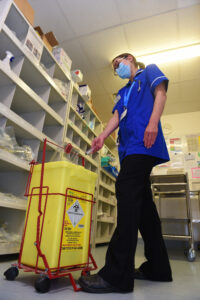 Deputy sister nurse putting needle into large yellow sharps bin