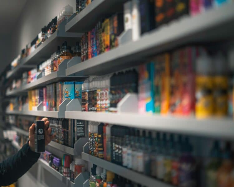 A hand reaching up to shelves containing a range of e-liquids