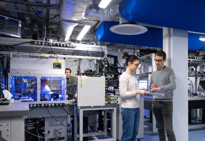 People working and talking in a lab filled with electrical and laser equipment
