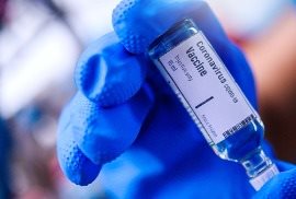 Blue gloved hand holding bottle of vaccine