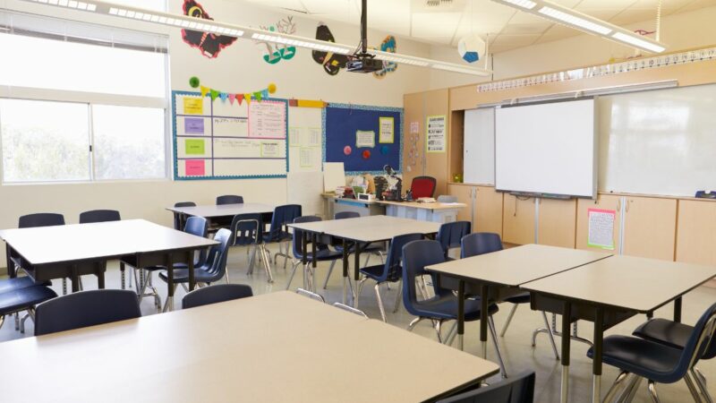 An empty school classroom, with desks and whiteboard at the front of the classroom