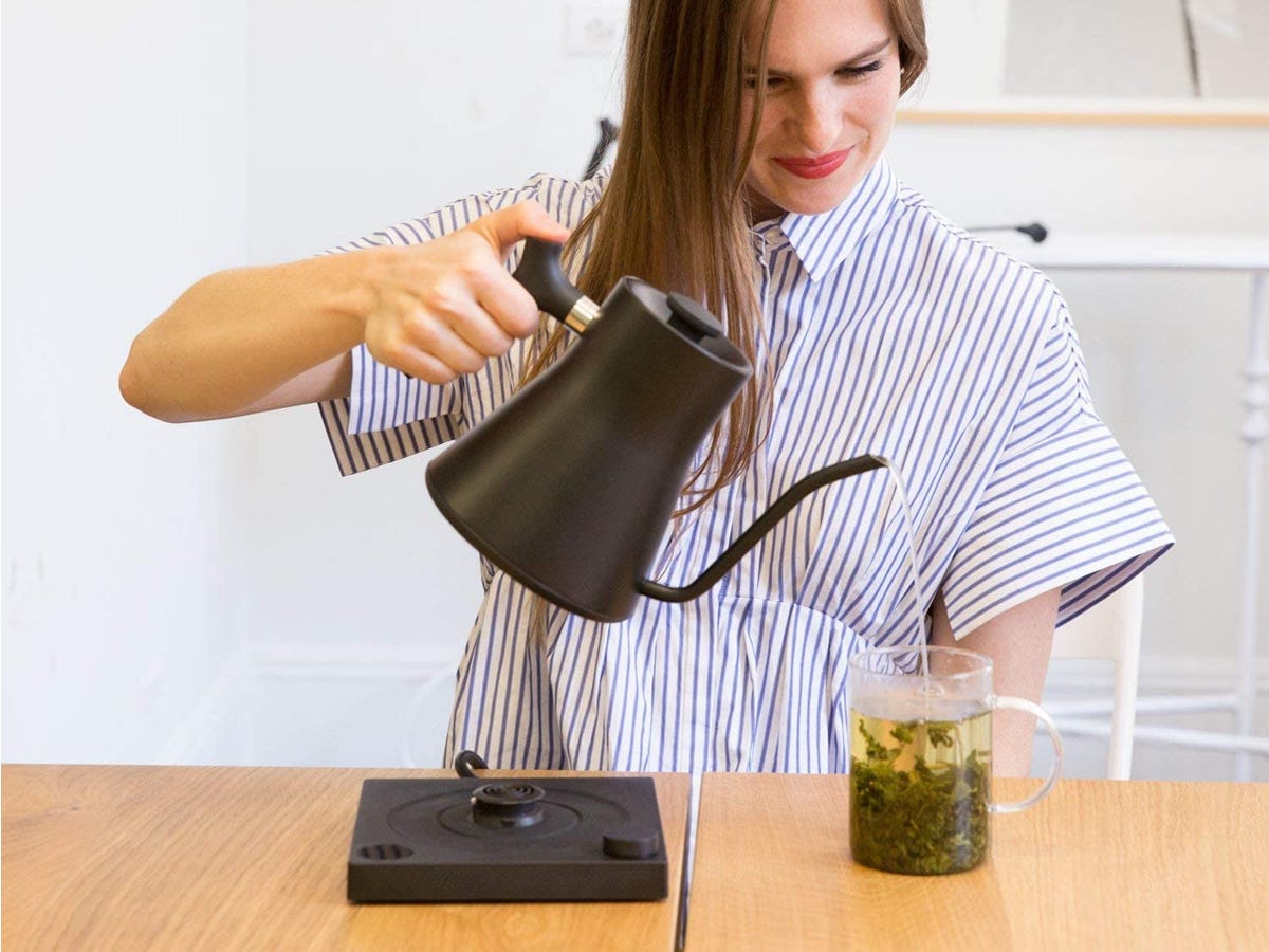 A person using the Fellow Stagg EKG Electric Pour-Over Kettle to fill a glass cup of tea with hot water