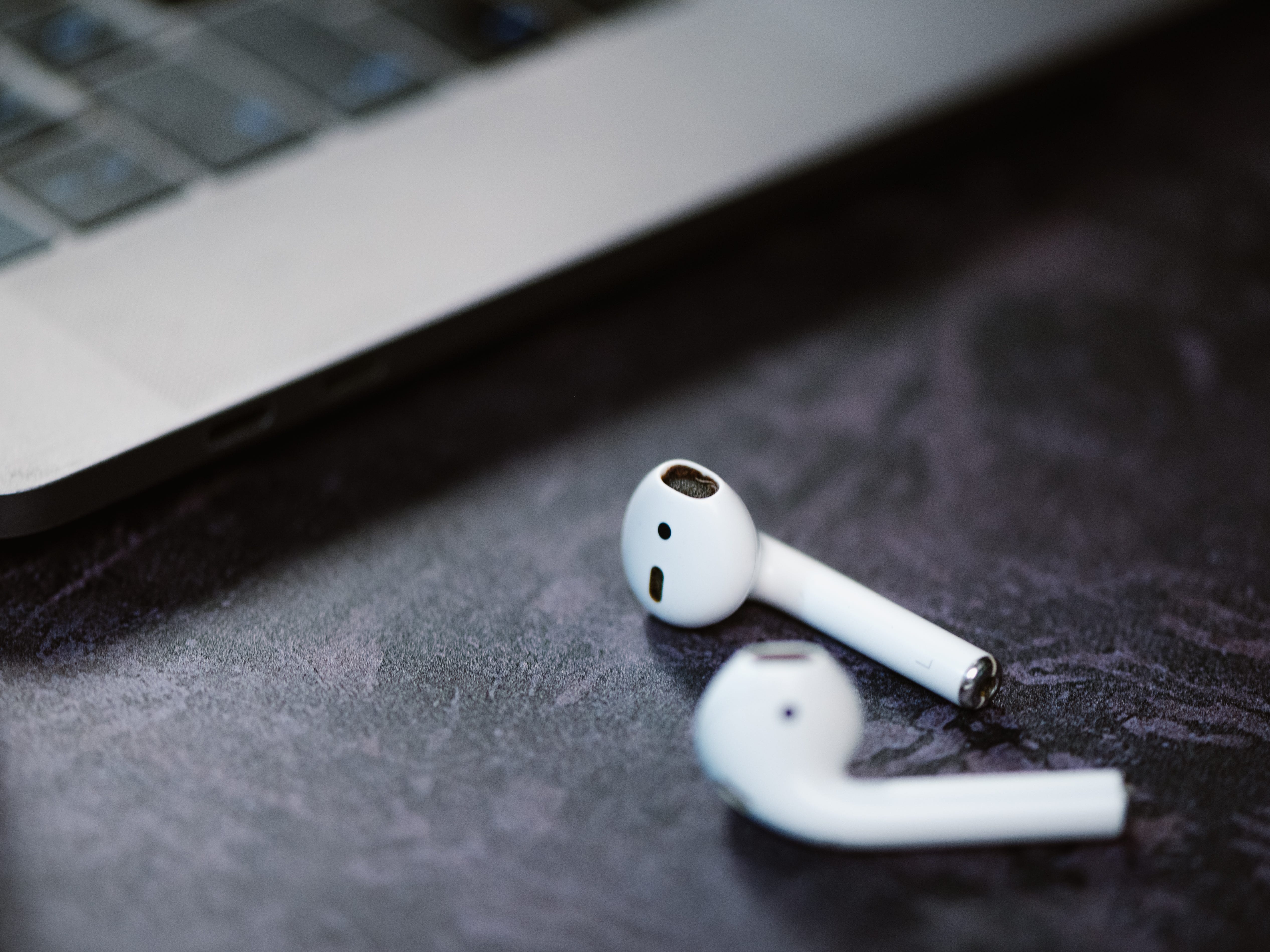 A pair of white Airpods on a desk next to a laptop computer.