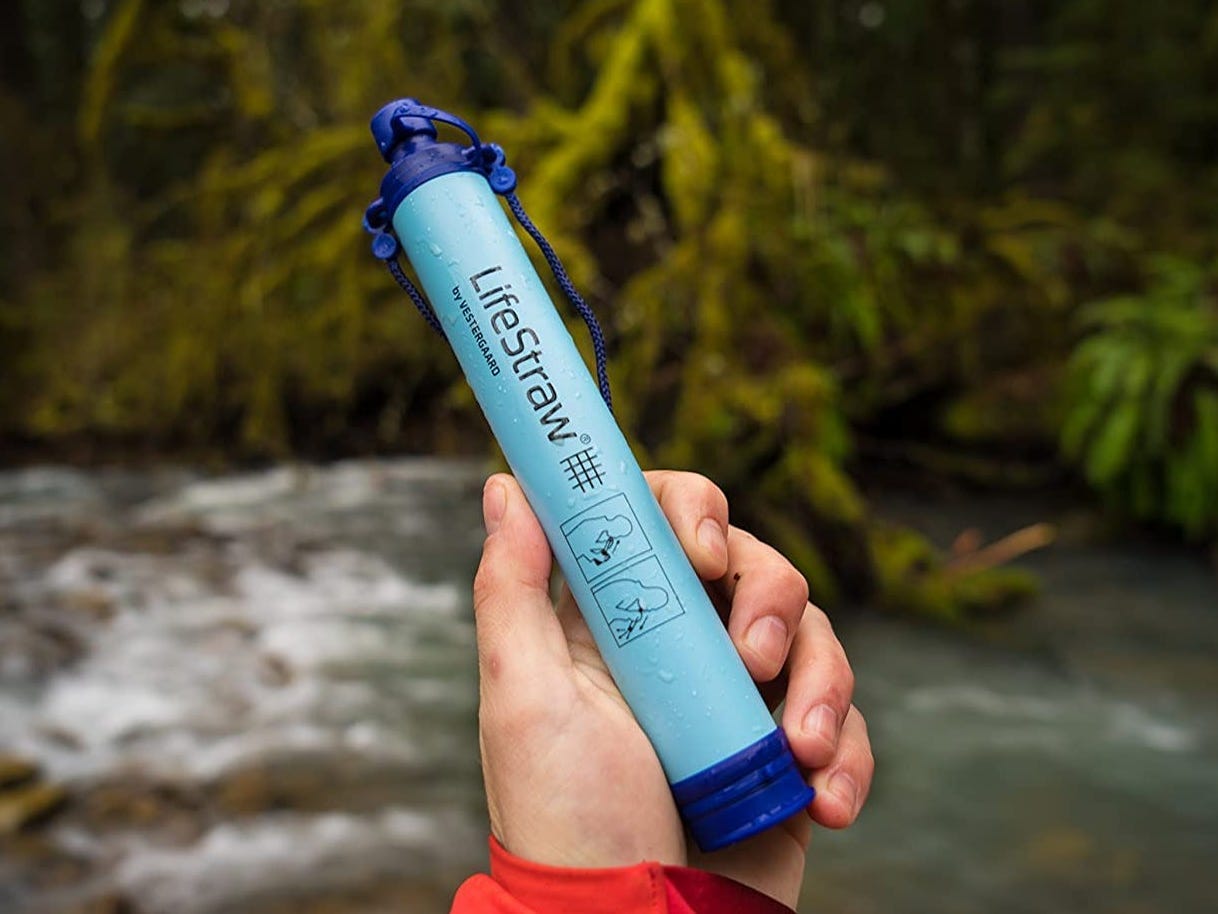 LifeStraw shown in someone's hand against the background of a creek