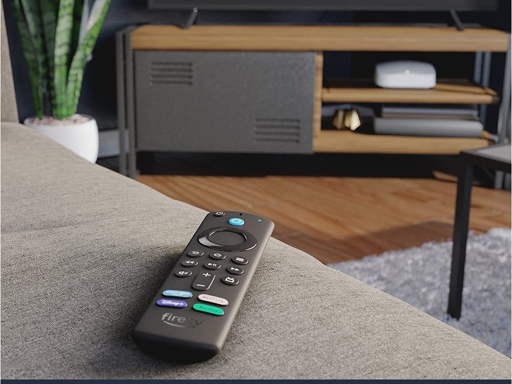 Amazon Fire TV Stick 4K remote resting on a couch in front of a tv in a living room