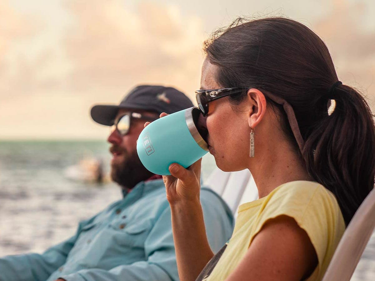 Person drinking from a  YETI Rambler Wine Tumbler while sitting on a beach at sunset.