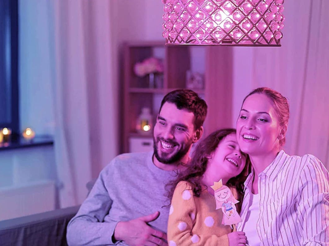 A family of three sitting in a living room under ceiling light fitted with a pink lightbulb