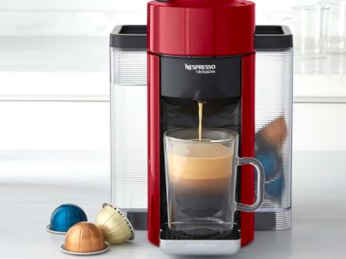 A Nespresso Vertuo by De'Longhi on a kitchen counter in the process of pouring a espresso drink into a clear mug.