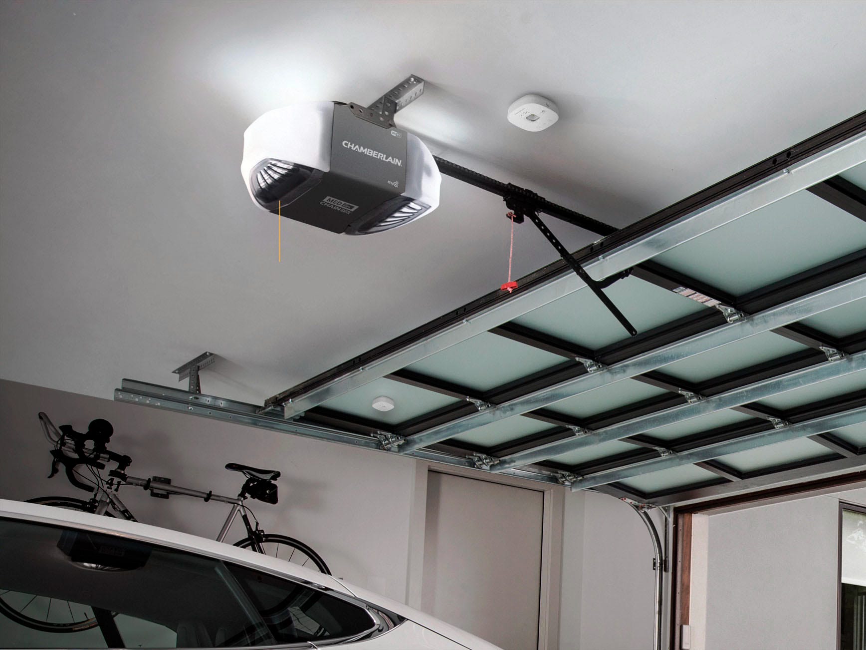 a Chamberlain myQ Smart Garage Door Opener (G0401) sits on the ceiling of a garage with a car inside and the door open