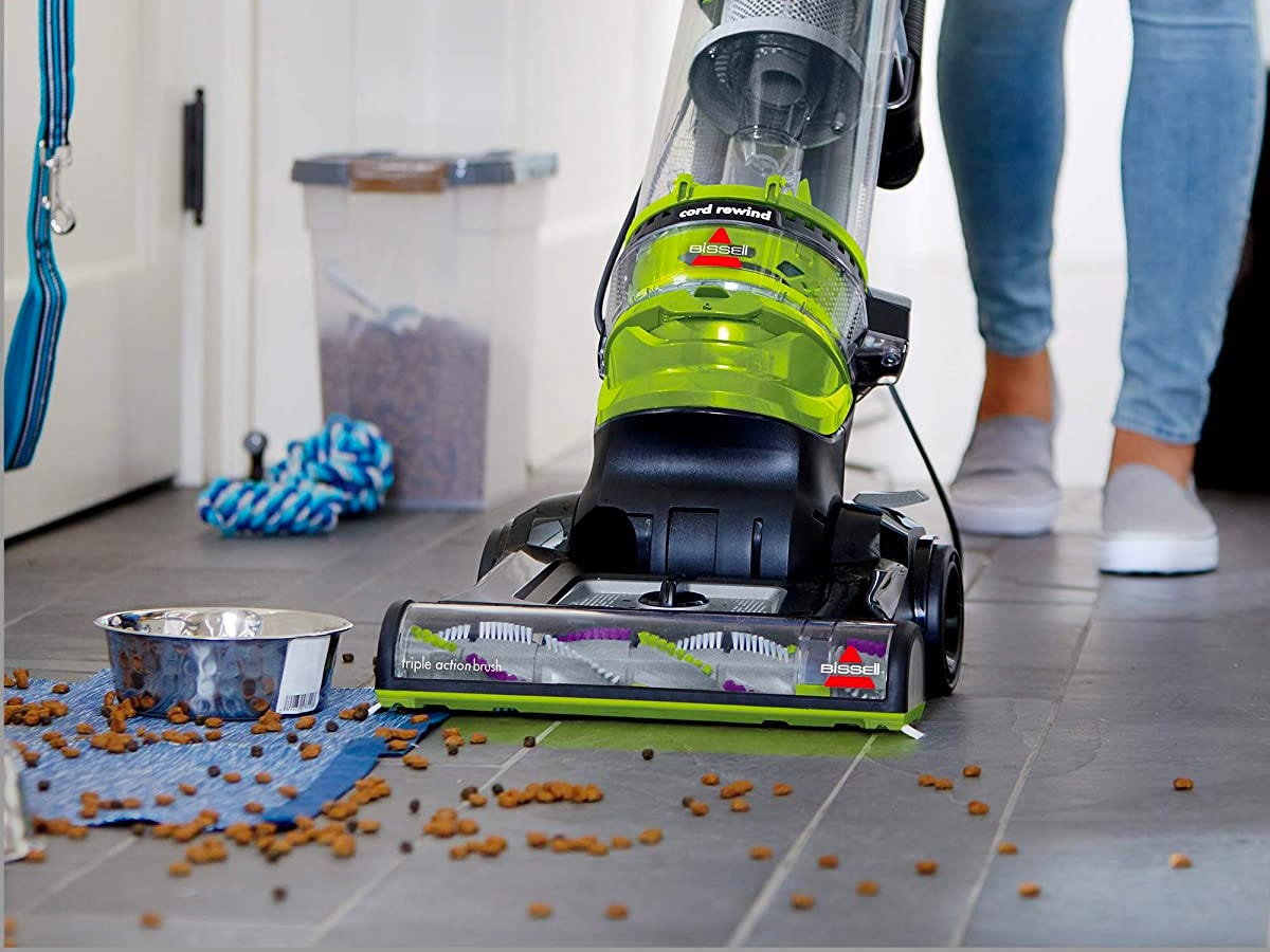 BlacA Bissell Cleanview Rewind Pet Deluxe Upright Vacuum Cleaner being used to clean up pet kibble spilled on the floor.