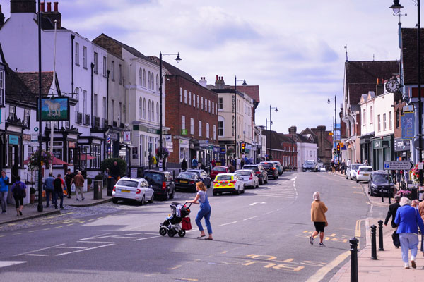 Colour photo of Dorking High Street, looking west, with cars on the road and pedestrians on pavements