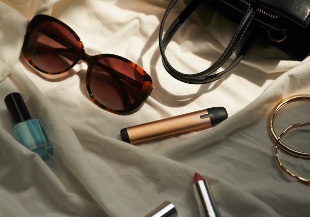 a pair of sunglasses, lipstick, and a purse on a bed