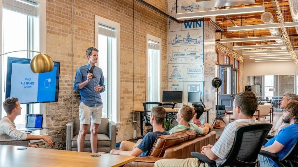 A team leader talking to a team sitting on a couch and in chairs, discussing the benefits of RFP automation.