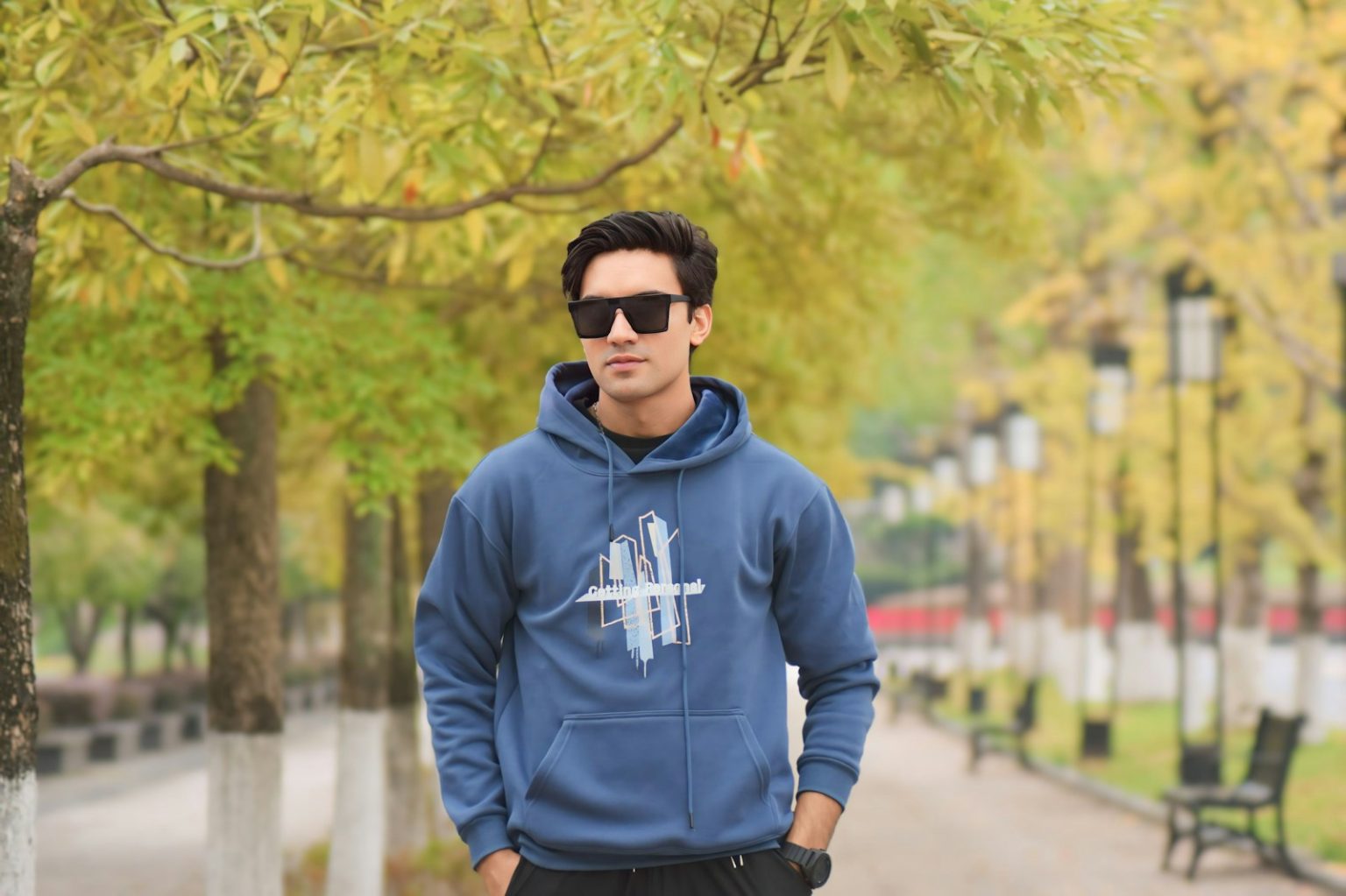 A man in a blue hoodie standing next to a tree
