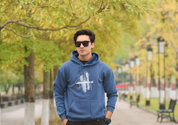 A man in a blue hoodie standing next to a tree
