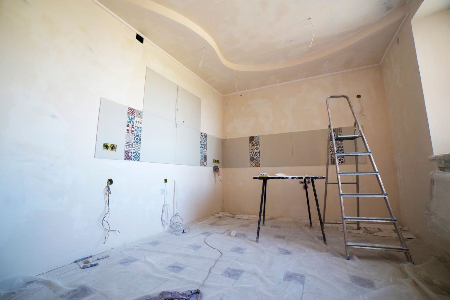 Renovate or Relocate: How to Choose the Right Option for Your Family A room mid-renovation with bare plaster walls, a stepladder and dust sheets on the floor