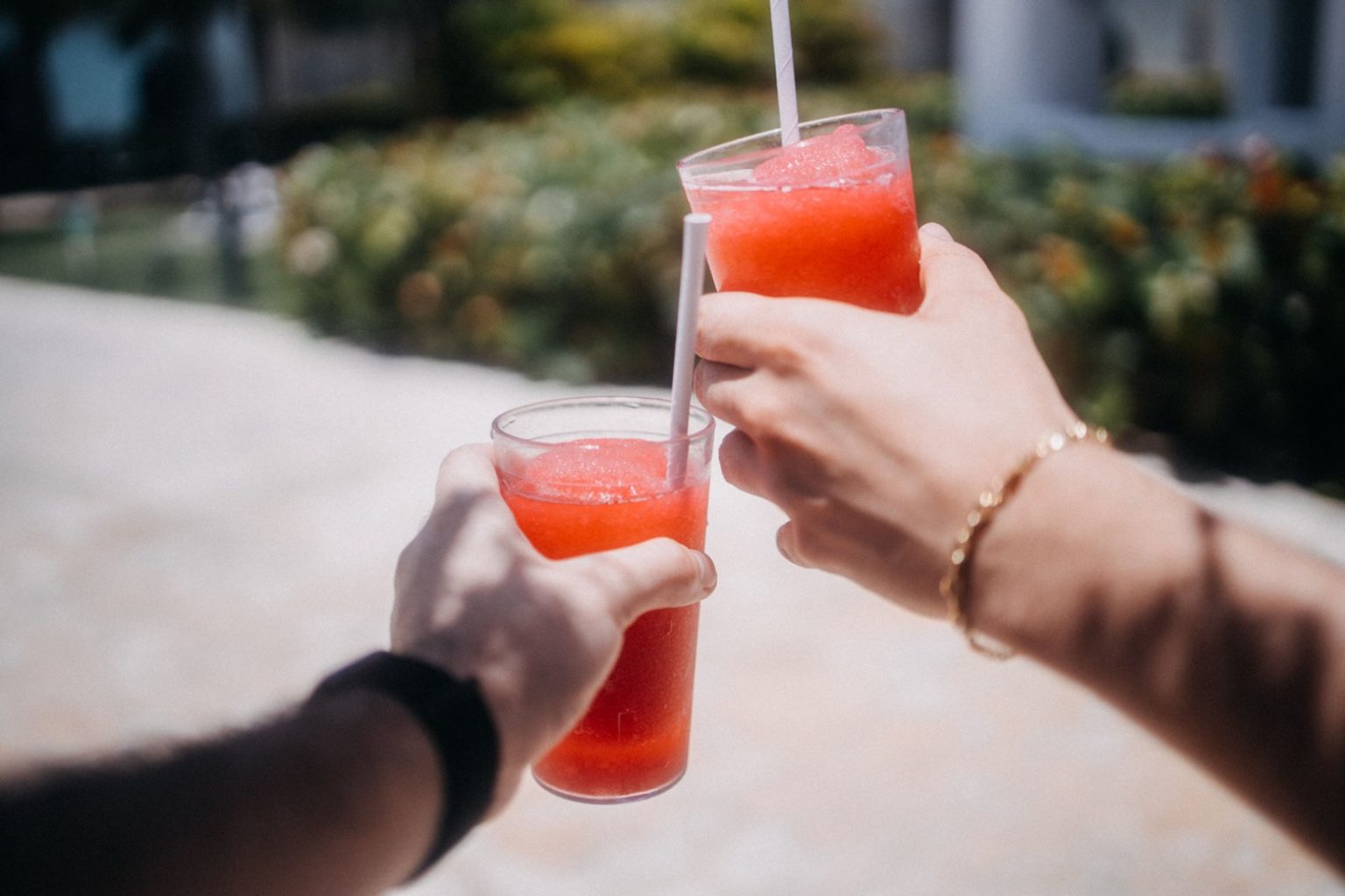 Two people clinking red slushy drinks outdoors